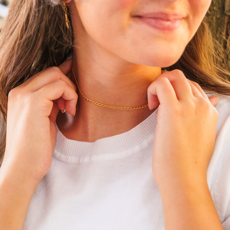 A close-up lifestyle photo of a woman wearing a delicate, fine gold curb link permanent chain as a simple necklace.