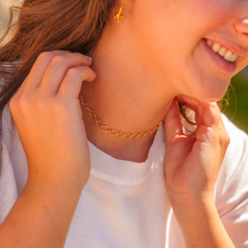 A close-up lifestyle shot of a woman smiling, wearing a gold interlocking round thick link permanent jewelry chain as a choker necklace.