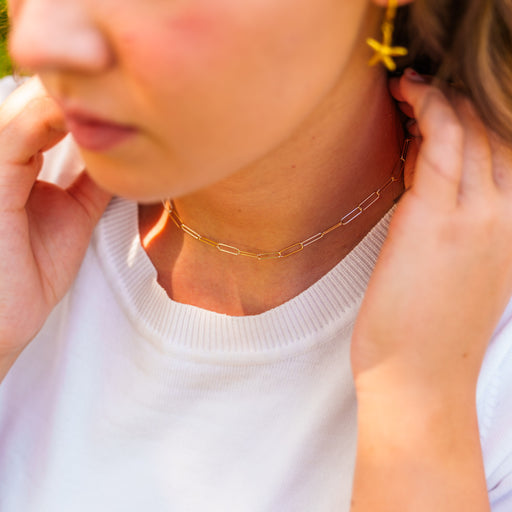 A close-up lifestyle shot of a woman wearing a delicate alternating gold and silver elongated paperclip link permanent jewelry necklace, paired with a matching gold starfish dangle earring.