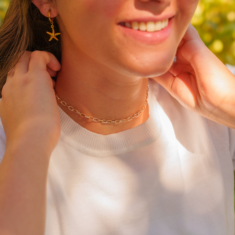 A close-up lifestyle shot of a woman smiling, wearing the Nelly permanent jewelry chain as a mixed metal pj necklace with alternating paperclip links.